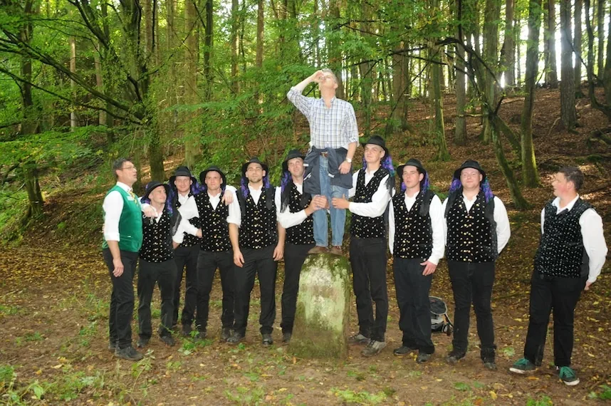 Die Grenzgangburschen am Grenzstein im Wald, einer steht oben auf dem Stein